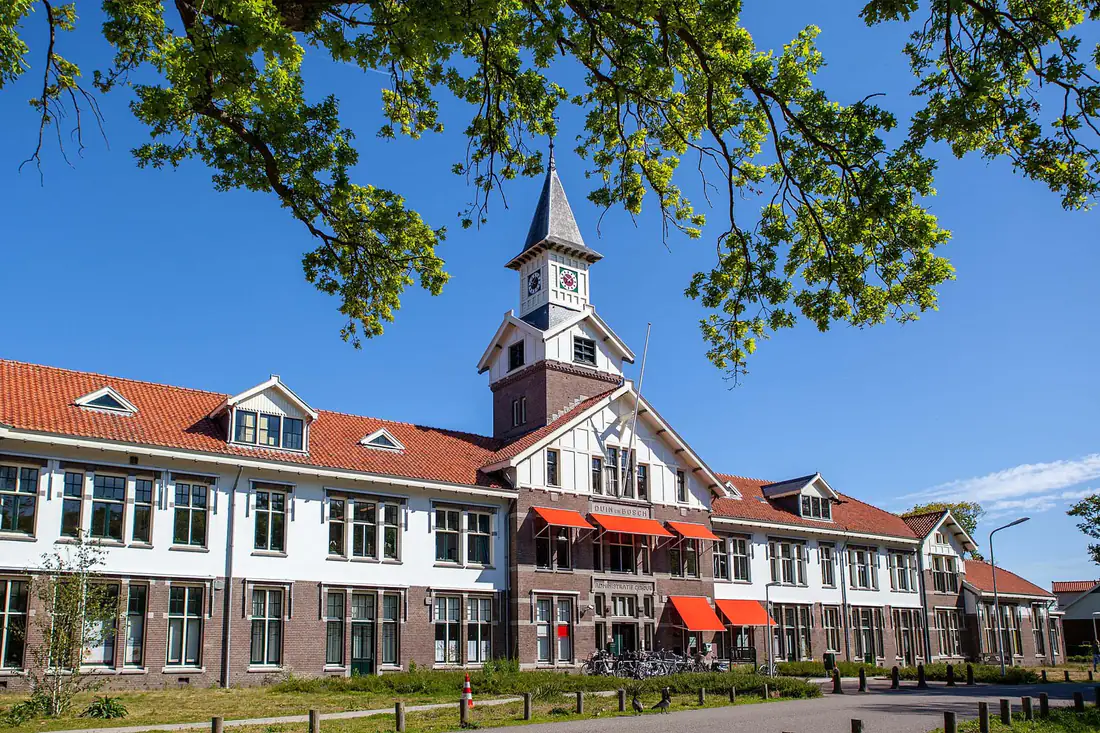 Het voormalige administratiegebouw van Duin en Bosch in Castricum, een wit-bruin pand met rode daken en een klokkentoren, met bomen op de voorgrond